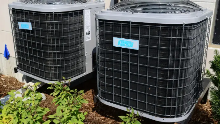 Air conditioning units installed outdoors, surrounded by greenery, highlighting HVAC maintenance and repair services by The Darville Company.