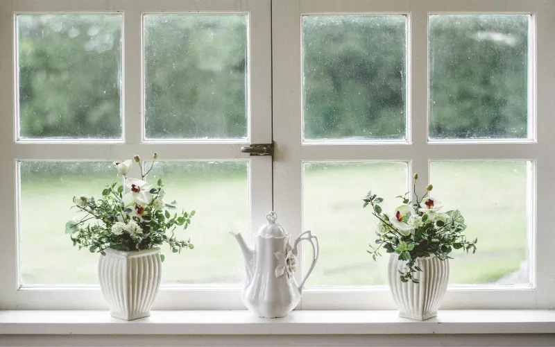 White teapot and two flower arrangements in vases on a window sill, suggesting home comfort and aesthetics in a domestic setting.