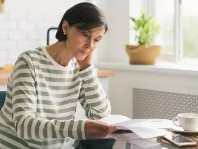 Woman sitting at a kitchen table, looking concerned while reviewing documents, reflecting on high water bills potentially indicating a water leak.