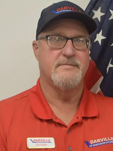 Jan Futrell, HVAC technician at The Darville Company, wearing a red uniform with a name tag, standing in front of an American flag backdrop.