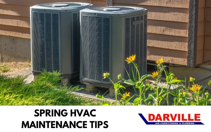 Two HVAC units by a wall with grass and flowers, showcasing spring maintenance tips from Darville Air Conditioning.