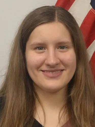 Emy Carpenter, team member at The Darville Company, smiling in front of a flag, representing the office support role in plumbing and HVAC services.