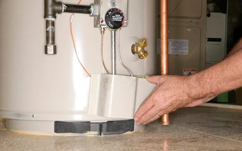 Hand adjusting a water heater component, showcasing maintenance work related to plumbing and HVAC services provided by The Darville Company.