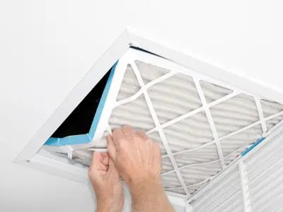 Hands replacing an air filter in a ceiling vent, emphasizing indoor air quality maintenance and HVAC system care.