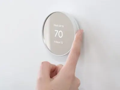 Hand adjusting a smart thermostat displaying temperature settings, illustrating energy efficiency and home comfort for HVAC optimization.