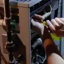 Hands performing maintenance on HVAC equipment, highlighting cables and tools in dim lighting. Chad's AC Direct services.