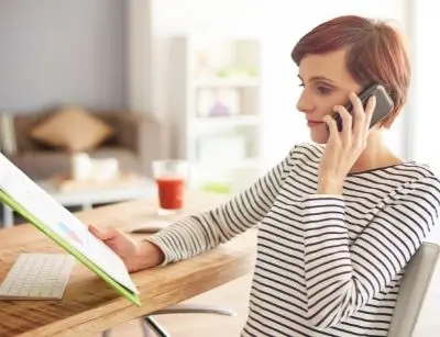 Woman on phone reviewing documents at a desk, emphasizing the importance of research for hiring HVAC contractors.