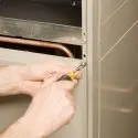 Person using a screwdriver to perform maintenance on a heating system, emphasizing HVAC service and repair expertise relevant to home comfort.