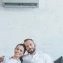 Couple relaxing indoors with a wall-mounted air conditioning unit, highlighting the importance of HVAC systems for home comfort.