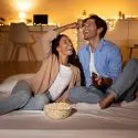 Couple enjoying a movie night with popcorn and remote in a cozy setting, highlighting HVAC comfort from Chad's AC Direct.