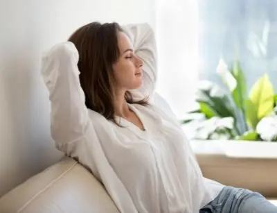 Woman relaxing on a couch with a peaceful expression, surrounded by indoor plants, emphasizing the importance of indoor air quality for health and wellness.