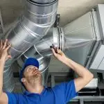 Technician adjusting ventilation ducts in a brightly lit HVAC service environment at Chad's AC Direct.