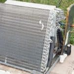 Cooling unit on concrete base with grass, featuring metal fins and coils, representing Chad's AC Direct HVAC services.
