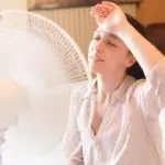 Woman feeling heat relief from a fan, illustrating summer HVAC needs for air conditioning at Chad's AC Direct.