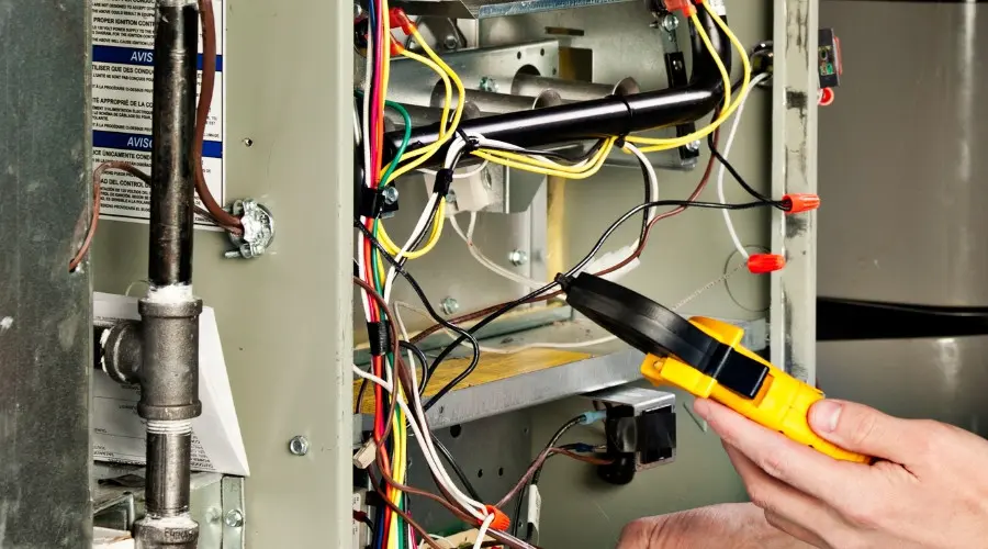 Technician inspecting heating system components with a multimeter, emphasizing the importance of fall maintenance for reliable performance and efficiency.