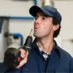 Man in work attire using a power drill in an industrial setting, showcasing HVAC service expertise at Chad's AC Direct.