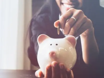 Woman smiling while inserting a coin into a white piggy bank, symbolizing savings and financial management.