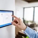 A person adjusting a digital thermostat displaying 22&deg;C in a modern home, highlighting HVAC control and comfort.