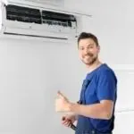 HVAC technician in a blue shirt thumbs-up with tools and an air conditioning unit at Chad's AC Direct.