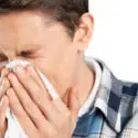 Young man experiencing allergy symptoms, sneezing into a tissue, highlighting the importance of air quality and dehumidifiers for allergy relief.