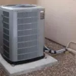 Air conditioning unit with grey metal casing on concrete base, surrounded by pea gravel near Chad's AC Direct HVAC services.