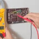 Hand holding a yellow multimeter measuring thermostat readings for HVAC maintenance at Chad's AC Direct.