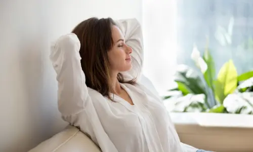 Woman relaxing indoors with arms behind her head, surrounded by indoor plants, illustrating improved indoor air quality and comfort.