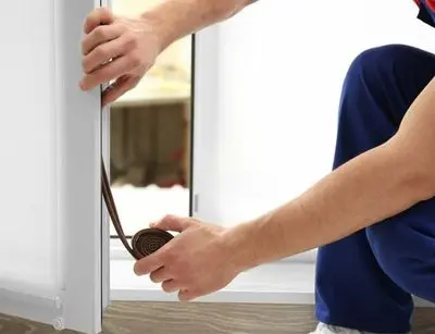 Person installing weatherstripping around a window to prevent drafts and improve home energy efficiency.