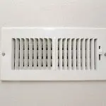 White plastic vent cover with horizontal slats affixed to a wall, illustrating practical home HVAC infrastructure.