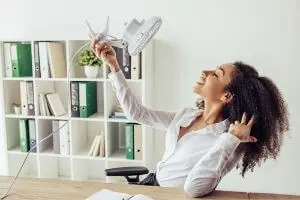 Woman enjoying a desk fan in a bright office, illustrating comfort during warm months, relevant to HVAC tips for maintaining indoor temperatures.