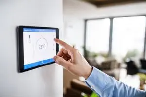 Person adjusting a digital thermostat displaying 23&deg;C, emphasizing HVAC control for improved indoor air quality and comfort.