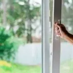 A hand opening a window, framed in white, with greenery visible outside, showcasing indoor air quality improvement.