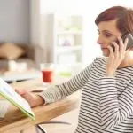 Woman on the phone in a home office with a notebook, promoting HVAC services at Chad's AC Direct.