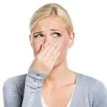 Young woman in a light gray cardigan covering her nose, illustrating discomfort, against a plain white background.