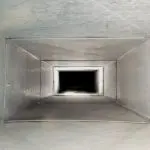 Vertical ventilation duct with reflective metal surfaces, depicting duct interior and HVAC maintenance themes.