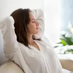 Woman relaxing on a comfortable sofa with indoor plants and natural light, showcasing HVAC comfort in a serene setting.
