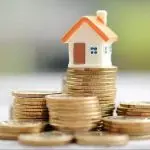White house model with orange roof and stacked coins representing HVAC investment and energy-efficient home upgrades.