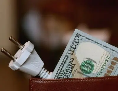 Electric plug and hundred-dollar bill in a wallet, symbolizing increased energy costs and HVAC efficiency concerns for homeowners.