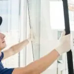 Window cleaner in blue uniform uses a squeegee on a modern window, emphasizing cleanliness and professionalism.