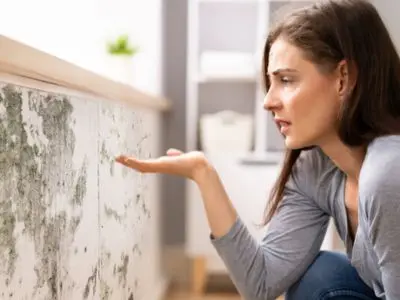 Woman inspecting mold growth on a wall, highlighting signs of excess moisture in a home, relevant to the need for a dehumidifier.