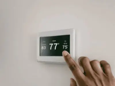 Hand adjusting a digital thermostat displaying temperature settings, emphasizing the importance of checking thermostat functionality for HVAC system efficiency.