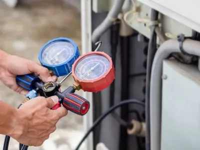 Technician using pressure gauges on an air conditioning unit to check refrigerant levels and diagnose airflow issues.
