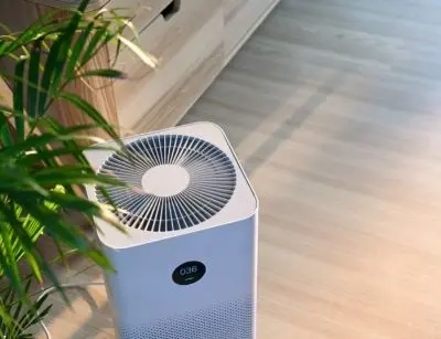 Air purifier in a modern interior setting, featuring a digital display and surrounded by indoor plants, illustrating air quality improvement solutions related to HVAC systems.