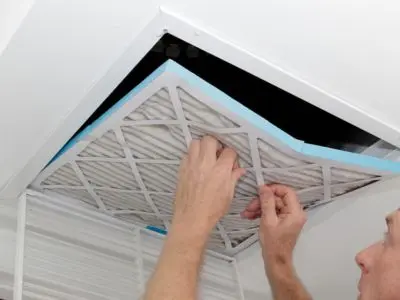 Person replacing a dirty air filter in a ceiling HVAC unit, emphasizing the importance of clean filters for heating system efficiency and safety.
