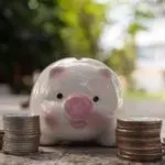 Piggy bank with stacked coins in an outdoor setting, representing savings and financial planning with Chad's AC Direct.