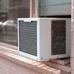Air conditioning unit on a window sill, showcasing its white exterior and grilled front for airflow, by Chad's HVAC services.