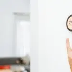 Hand reaching for a minimalist wall clock in a cozy interior, emphasizing the need for HVAC efficiency and comfort.