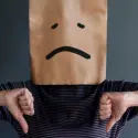 Person with a paper bag over their head, sad face, and thumbs-down gesture, indicating HVAC service disappointment.