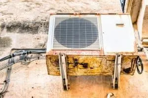 Rusty air conditioning unit mounted on a wall, showcasing signs of wear and tear, relevant to HVAC maintenance and repair discussions.