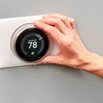 A person adjusting a sleek thermostat display showing 78&deg;F, promoting energy management for Chad's AC Direct HVAC services.